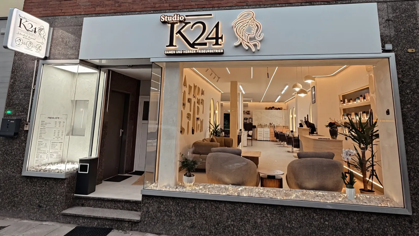 Außenansicht von Studio K24 an der Frintroper Straße 423 in Essen: beleuchtetes Ladenschild und Blick durch das Schaufenster in den Salon